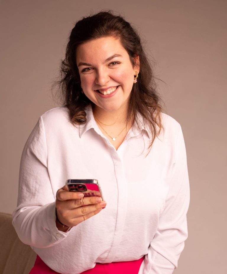 Portrait von Linn Gauda, junge Frau mit weißer Bluse, dunklen Haaren und Handy in der Hand
